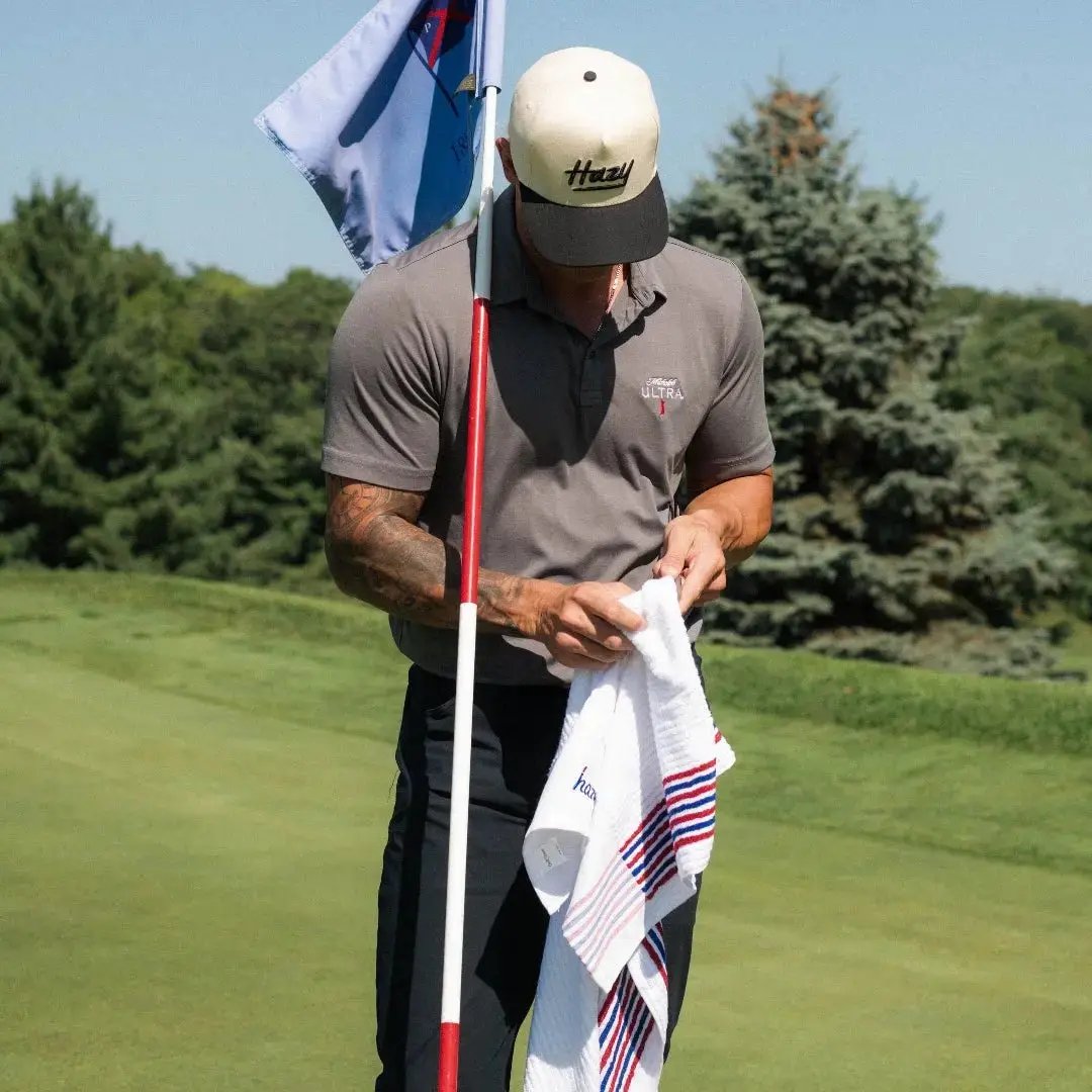 Man on a golf course holding a flag and towel with a clear blue sky and trees in the background