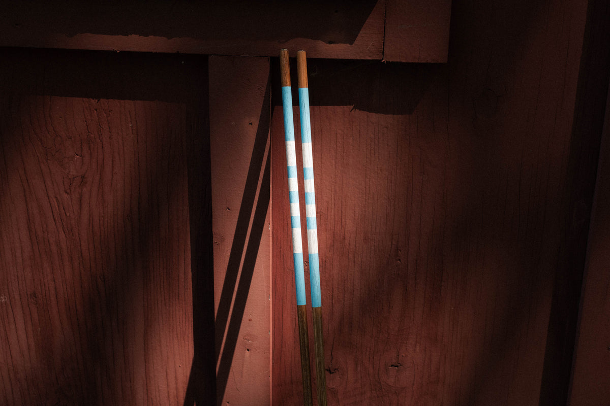 Hand-finished blue and white Hazy Golf alignment sticks against a wooden clubhouse wall.
