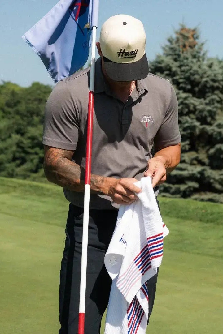 Man on a golf course holding a flag and towel with a clear blue sky and trees in the background