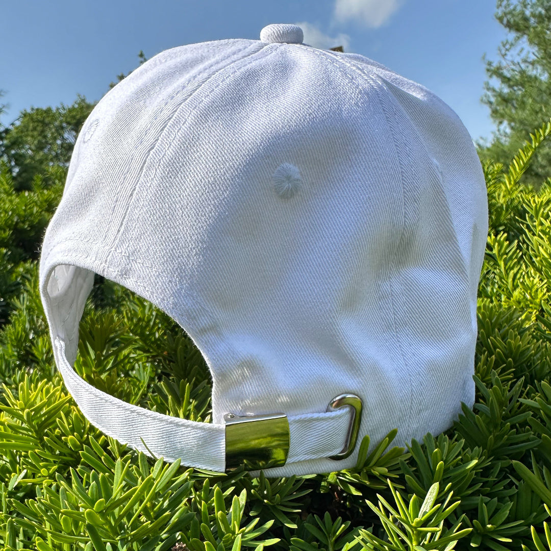 White cap with a metal buckle on green foliage