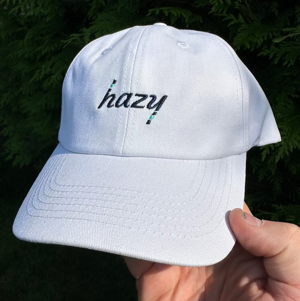 White cap with 'hazy' text held by a hand against a dark background